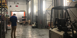 A consultant taking ethylene readings in a produce warehouse with visible forklifts, storage racks, and fluorescent lighting.